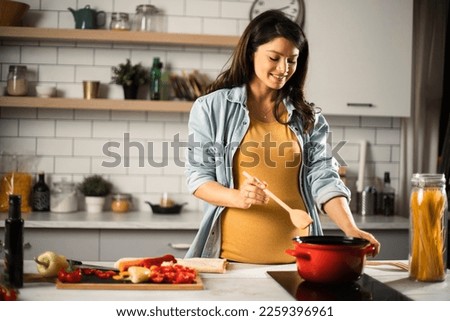 Beautiful pregnant woman preparing delicious food. Smiling woman cooking at home. Royalty-Free Stock Photo #2259396961
