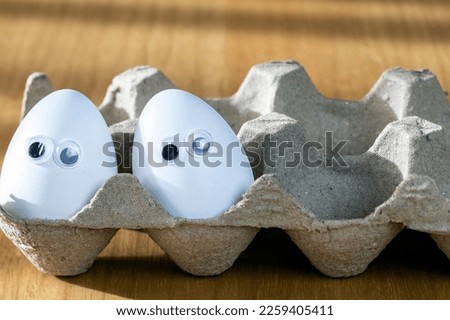 Funny faces on white eggs in carton box with organic chicken eggs on kitchen table closeup big animation eyes. humor, food and easter holiday concept.