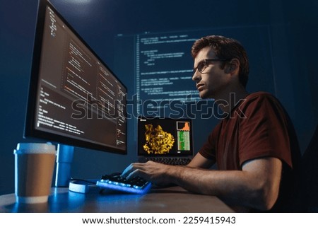 Side view portrait of modern IT developer using computer at home office at night, working on software, coding new application, sitting in front of big pc monitor. Data science specialist at work Royalty-Free Stock Photo #2259415943
