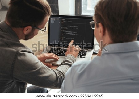 IT specialist giving personal programming lesson to man. Over shoulder view of coders colleagues working on new project together Royalty-Free Stock Photo #2259415945