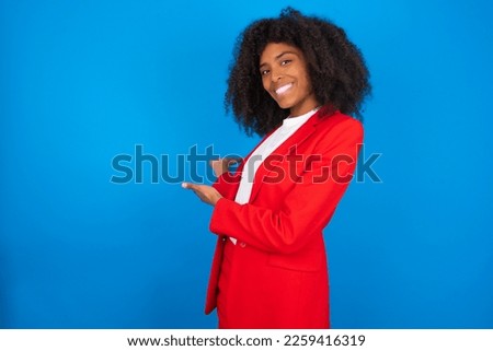 young businesswoman with afro hairstyle wearing red over blue wall Inviting to enter smiling natural with open hands. Welcome sign.