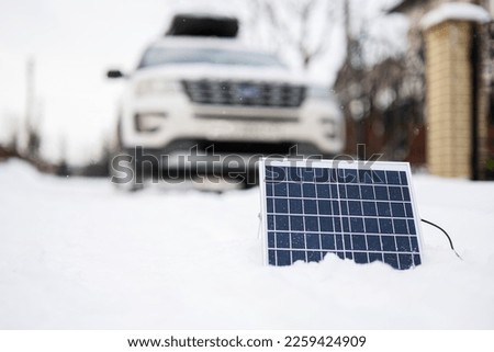 Portable solar panel against SUV car at winter.