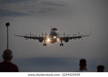 Plane spotters and landing airplane in the sunset,  people waiting, observing, recording, filming, taking photos, airliner, landing lights on, landing gear up, skiathos, greece, san maarten