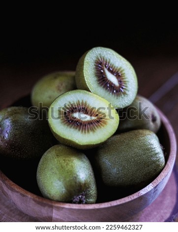  Red kiwi fruit in wooden bowl, on wooden table and dark background. Selective focus.