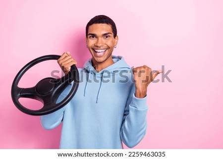Photo of funny positive satisfied guy enjoy rent automobile service hold steering wheel direct finger empty space isolated on pink color background