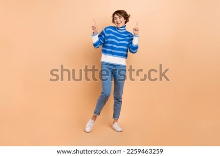 Full length photo of excited funky woman dressed striped sweater having fun pointing empty space isolated beige color background