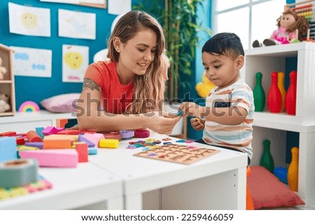 Teacher and toddler playing with maths puzzle game sitting on table at kindergarten Royalty-Free Stock Photo #2259466059