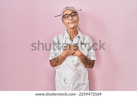 Middle age woman with grey hair wearing artist look smiling with hands on chest with closed eyes and grateful gesture on face. health concept. 