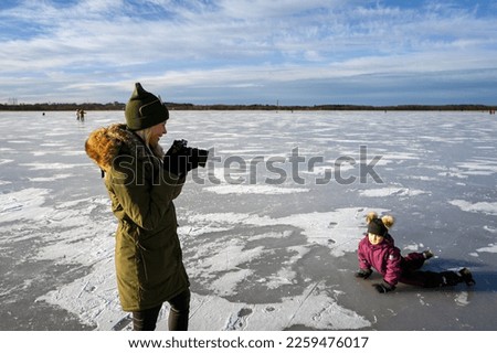 A girl photographs a little girl on an icy lake in winter.