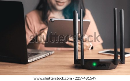 Selective focus at router. Internet router on working table with blurred happy woman using tablet at the background. Fast and high speed internet connection from fiber line with LAN cable connection.
