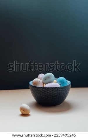 Easter at home. Bowl with colored easter eggs on the table with dark wall background. Minimalistic Easter vertical card. Selective focus. Copy space.