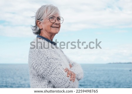 Portrait of pensive handsome senior woman standing by the sea looking away. Smiling elderly white-haired lady in outdoor excursion enjoying freedom, relax and retirement Royalty-Free Stock Photo #2259498765