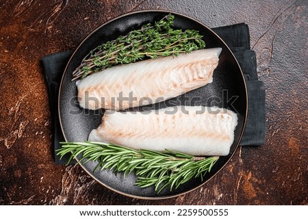 Raw cod loin fillet steaks with herbs on plate. Dark background. Top view.