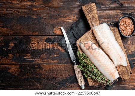 Cod fish fillets, raw codfish with thyme on wooden board. Wooden background. Top view. Copy space.