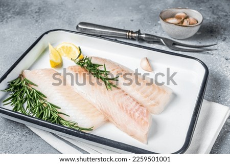 Uncooked Raw cod loin fillet steaks with herbs in kitchen tray. Gray background. Top view.