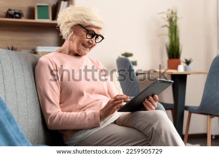 Senior woman using digital tablet while sitting at the sofa at home. Technologies and elderly people concept. Stock photo 