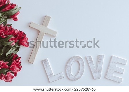 Small wood cross and word love on a white background with red flowers