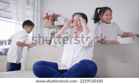 Kids tired and running near upset mother sitting at couch. Frustrating mom stressful feels heaviness and headache at home. Fatigue parent doesn't want to play with son and daughter Royalty-Free Stock Photo #2259530185