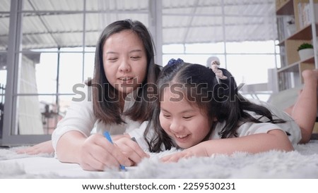 Front view of mom and kid lying on the floor doing painting by coloured pencils and talking together in living room with lots of happiness