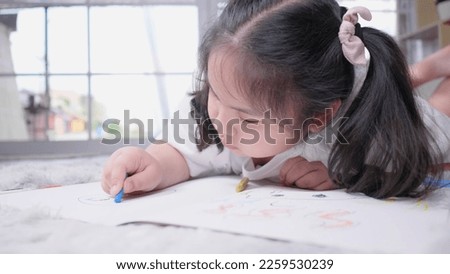 Front view of  kid lying on the floor doing painting by coloured pencils in living room with lots of happiness. Art activity at home
