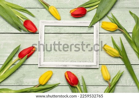 Composition with empty picture frame and beautiful tulip flowers on color wooden background. Hello spring