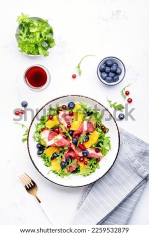 Gourmet salad with smoked duck, oranges, blueberries, cranberries, arugula and lettuce with red wine, white table background, top view
