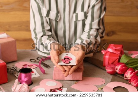 Woman with paper tag for gift at table, closeup. International Women's Day celebration