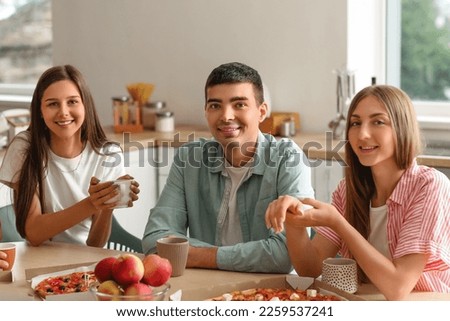 Group of friends with drinks and pizza at table in kitchen