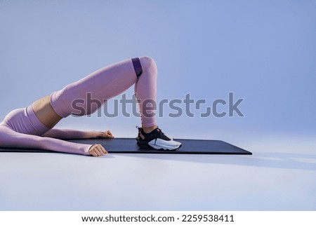 Athletic woman trains legs with fitness elastic band on studio background. High quality photo