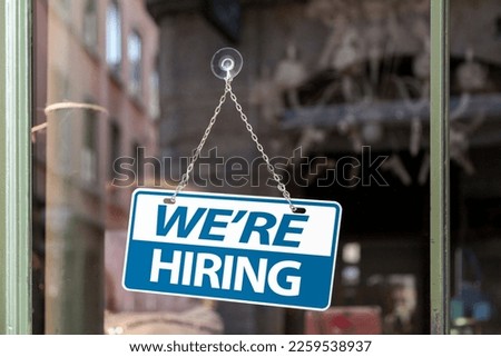 Close-up on a blue and white sign in a window with written in "We're hiring".