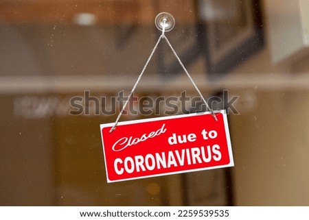 Red sign hanging at the glass door of a shop saying "Closed due to coronavirus".