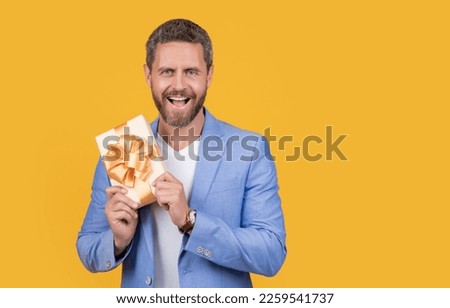 photo of surprised guy holding occasion gift box. guy hold gift box isolated on yellow background.
