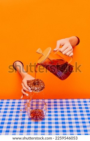 Food pop art photography. Female hand sticking out orange paper with kettle and pouring black tea over chocolate donut. Concept of taste, creativity, art. Complementary colors. Copy space for ad, text