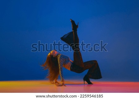 Portrait of young girl dancing, training heels dance in stylish clothes over blue background in neon light. Concept of dance lifestyle, modern style, contemporary, youth culture, self-expression Royalty-Free Stock Photo #2259546185