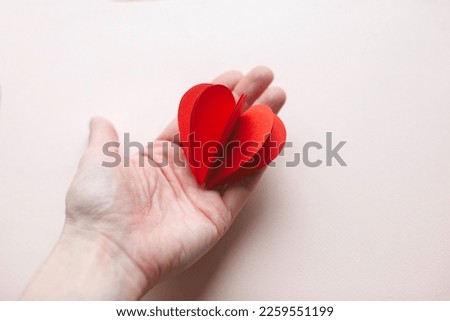 Handmade paper heart on hand. For valentine's day on pink background.