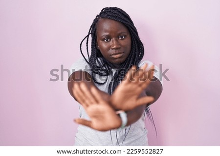 Young african woman standing over pink background rejection expression crossing arms and palms doing negative sign, angry face 
