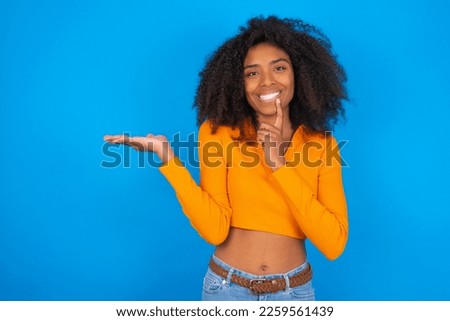 Positive Young beautiful girl with wearing orange crop top over blue background advert promo touch finger teeth