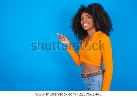 Profile photo of Young beautiful girl with wearing orange crop top over blue background indicate finger empty space offer