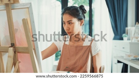 Happy youth Asia Female wear apron holding palette color use brush painting on canvas create artwork in cozy workshop at home. Contemporary Painter Abstract Modern Art, Creativity and people concept.