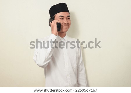 portrait of asian man communicating using cell phone or smartphone. Portrait of Indonesian man in white shirt and cap on isolated white background.
