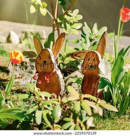 Handmade two wooden easter rabbit, decor stands in flower garden backdrop of the with copy space.