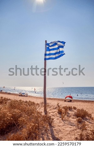 Greek national flag flies on a sandy beach of Corfu, a Greek island in the Mediterranean Sea
