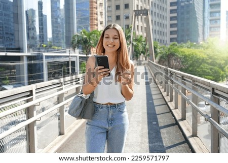 Young casual Brazilian woman watching her mobile phone walking in the city Royalty-Free Stock Photo #2259571797