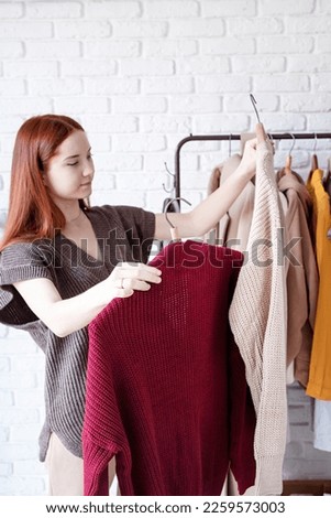beautiful young woman in trendy outfit standing in front of hanger rack and choosing outfit dressing. Selection of a wardrobe, stylist, shopping. Clothes designing Royalty-Free Stock Photo #2259573003