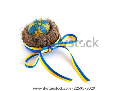 traditional Ukrainian Easter egg in national colors in the nest and a yellow-blue ribbon on a white background Royalty-Free Stock Photo #2259578029