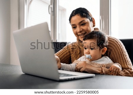 Stock photo of happy mother and her baby watching cartoons in the computer at home.