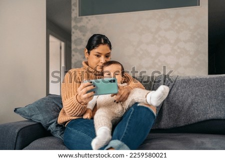 Stock photo of happy mother and her baby watching cartoons in the phone at home.