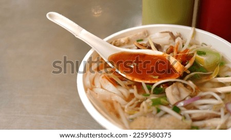 a bowl of chicken soup with a spoon full of chilli sauce.