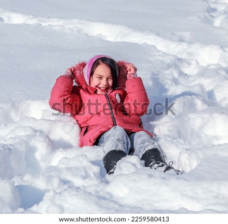 Happy little girl beauty in winter lies in the snow outdoors.