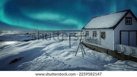 Winter landscape with White wooden house under a beautiful starry sky and Northern Lights on the shore of the North SeaÑŽ Lofoten islands. Norway. Travel adventure Lifestyle concept